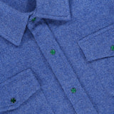 Close-up of the God’s True Cashmere Solid Cashmere Shirt featuring malachite-inspired green snap buttons, two chest pockets, and textured blue fabric. Part of a white label is visible at the top.