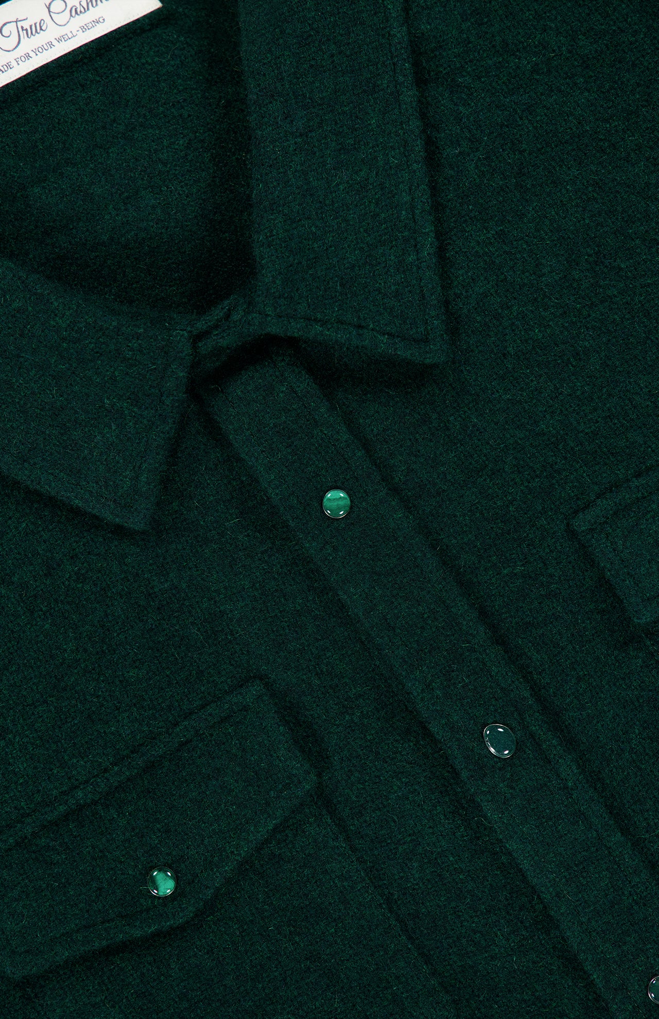 Close-up of the Solid Cashmere Shirt with Malachite Buttons by God’s True Cashmere, crafted from luxurious unisex cashmere in dark green, featuring two chest pockets with malachite buttons and a pointed collar.