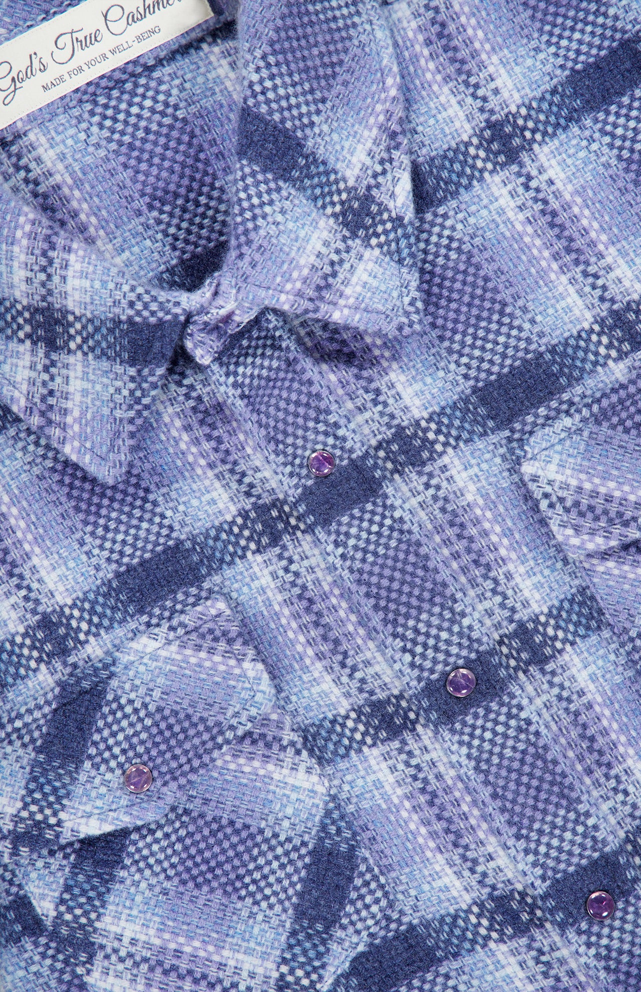 Close-up of a blue and purple plaid cashmere shirt by God’s True Cashmere. This unisex Plaid Cashmere Shirt with Amethyst Button features eye-catching amethyst gemstone snaps and chest pockets, elevating the classic blue plaid design with luxurious detail.