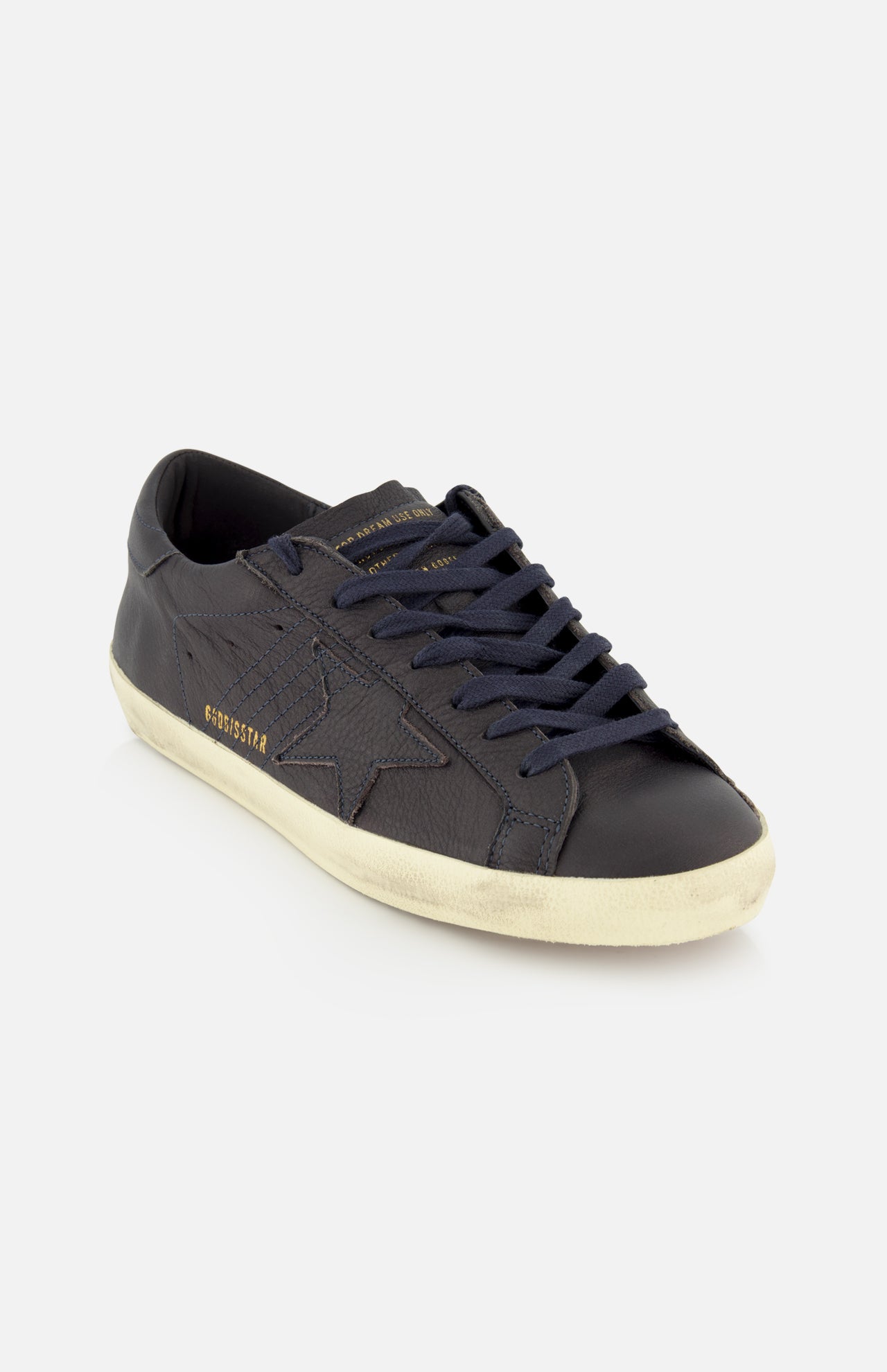 The GOLDEN GOOSE Super Star Leather Upper Sneaker is a dark navy low-top featuring a distinctive star design on the side, gold “GOLDENSTAR” text, black laces, and an off-white distressed sole. Styled against a plain white background, this contemporary pair reimagines classic navy sneakers with signature Golden Goose flair.