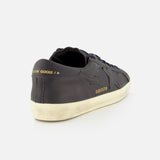 The Super Star Leather Upper Sneaker by GOLDEN GOOSE is shown from the back left angle against a white background, featuring a dark navy leather upper, a distressed sole, gold "GOLDEN GOOSE" text near the heel, and a star design on the side.
