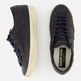 A pair of GOLDEN GOOSE Super Star Leather Upper Sneakers in navy blue with off-white, distressed soles is displayed from the side and top view, showcasing star accents and SUPER-STAR branding on the insole.
