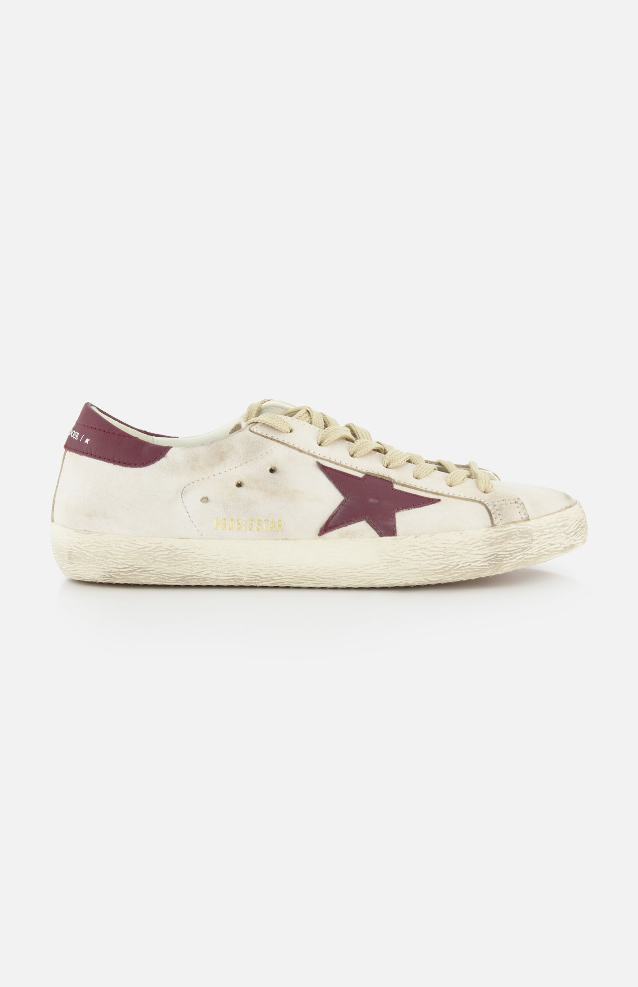 The GOLDEN GOOSE Super Star Leather Upper Toe And Tongue Sneaker features an off-white leather lace-up design with beige laces, a maroon star detail, GOLDENSTAR in gold, scuff marks, and a maroon heel tab for a signature distressed look.