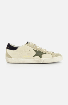 The GOLDEN GOOSE Super Star Nappa Upper Suede Sneaker features a beige upper, green side star, white laces, black heel tab, and a worn, distressed sole.