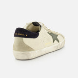 The GOLDEN GOOSE Super Star Nappa Upper Suede Sneaker, in beige with a dark green star, black heel tab with gold text, white laces, and a distressed sole, is displayed on a white background.