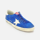 The GOLDEN GOOSE Super Star Suede Upper And Nylon Tongue Sneaker features a blue suede upper, white star, worn-effect white sole, and GOLDEN GOOSE branding on the side and tongue, with blue laces adding classic style.