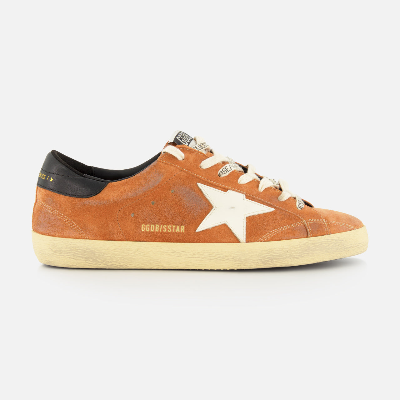 The GOLDEN GOOSE Super Star Suede Upper Toe And Tongue Sneaker features an orange suede upper with a white star logo, beige laces, a black heel tab, and a slightly scuffed beige sole—capturing the brand's signature distressed aesthetic. Displayed in side profile against a plain white background.