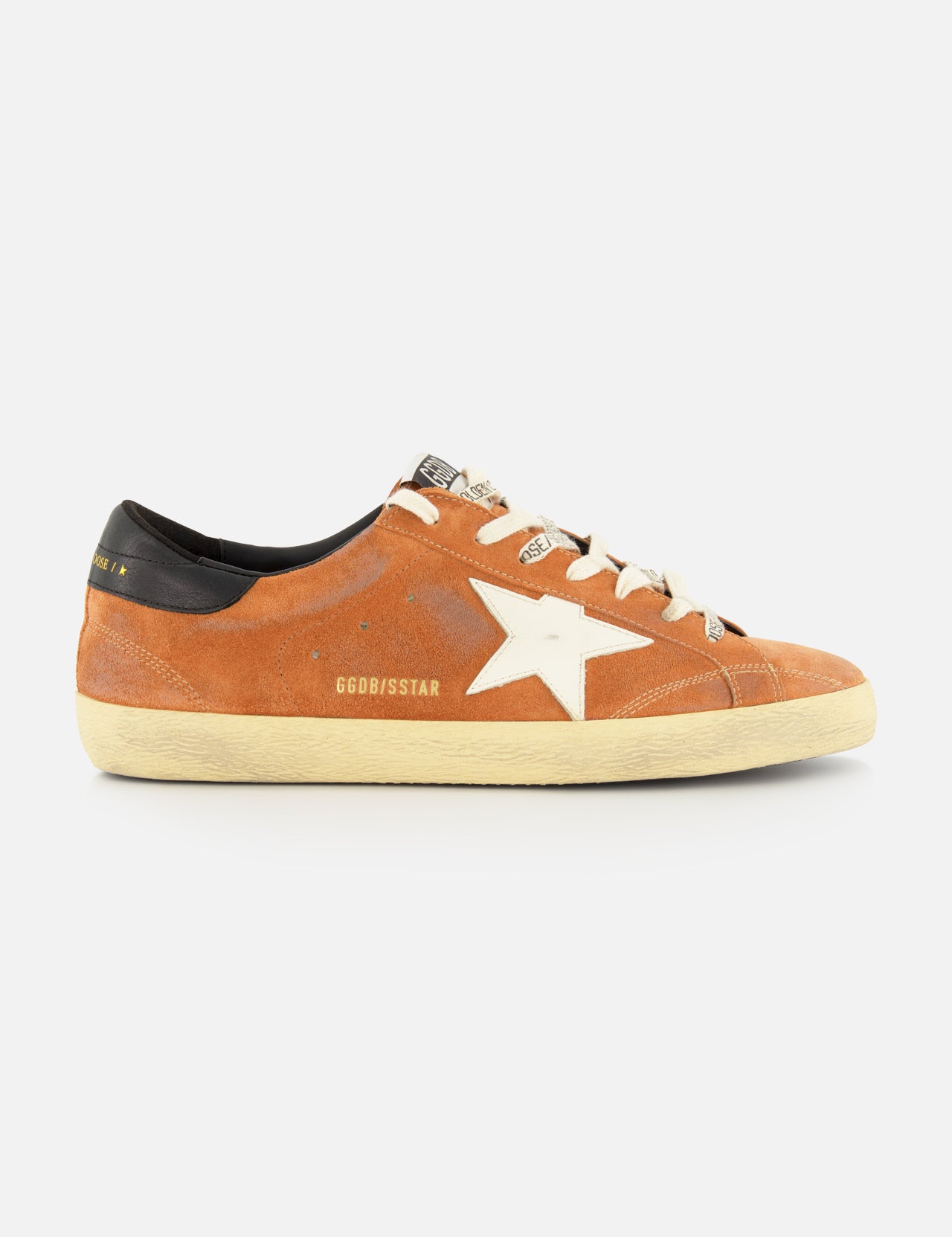The GOLDEN GOOSE Super Star Suede Upper Toe And Tongue Sneaker features an orange suede upper with a white star logo, beige laces, a black heel tab, and a slightly scuffed beige sole—capturing the brand's signature distressed aesthetic. Displayed in side profile against a plain white background.