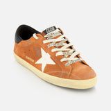 The Super Star Suede Upper Toe And Tongue Sneaker by GOLDEN GOOSE features a brown suede upper, a distinctive white star on the side, off-white laces printed with Golden Goose branding, a contrasting black heel tab, and a deliberately distressed sole that delivers their iconic worn-in aesthetic.