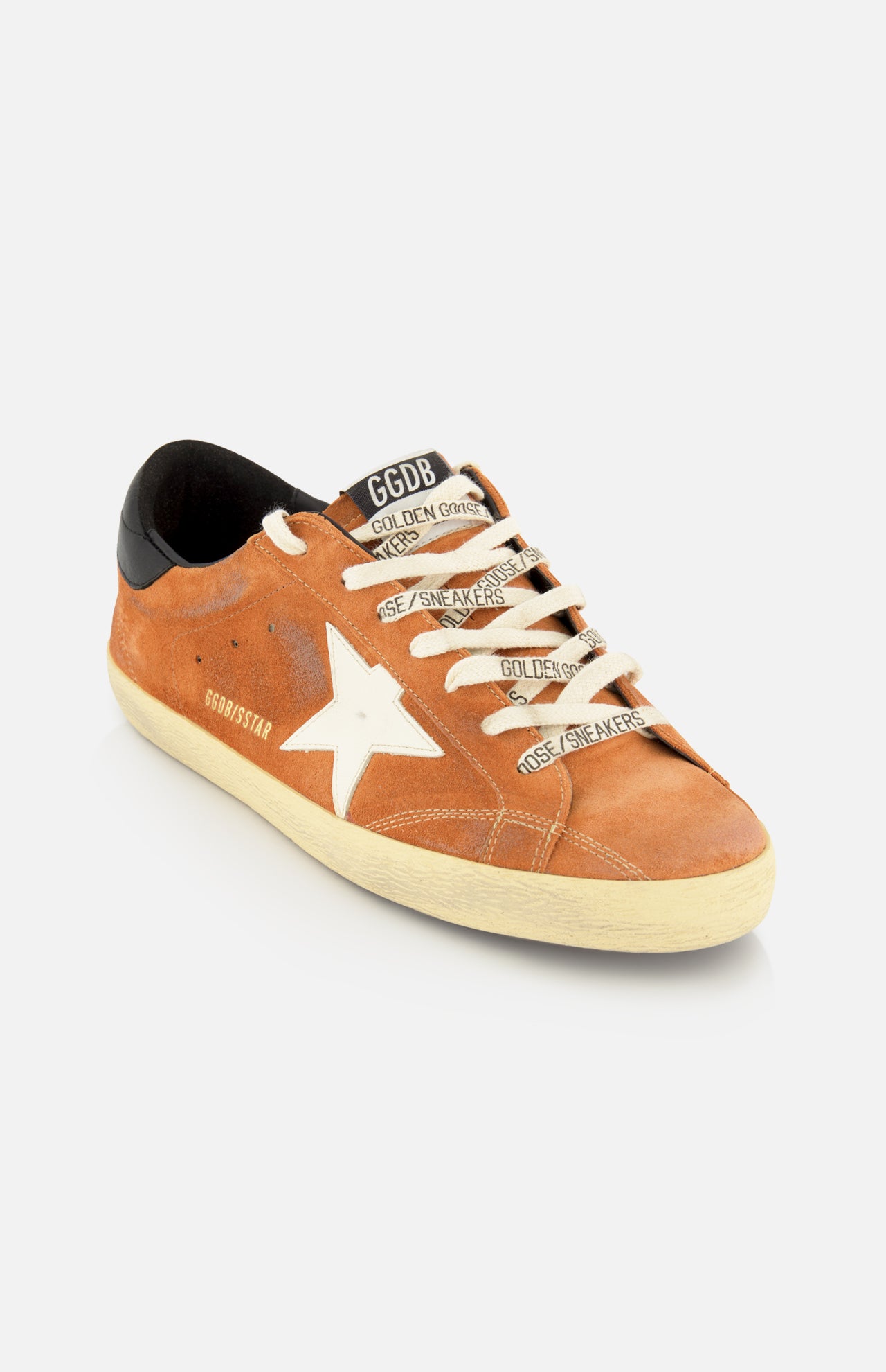 The Super Star Suede Upper Toe And Tongue Sneaker by GOLDEN GOOSE features a brown suede upper, a distinctive white star on the side, off-white laces printed with Golden Goose branding, a contrasting black heel tab, and a deliberately distressed sole that delivers their iconic worn-in aesthetic.