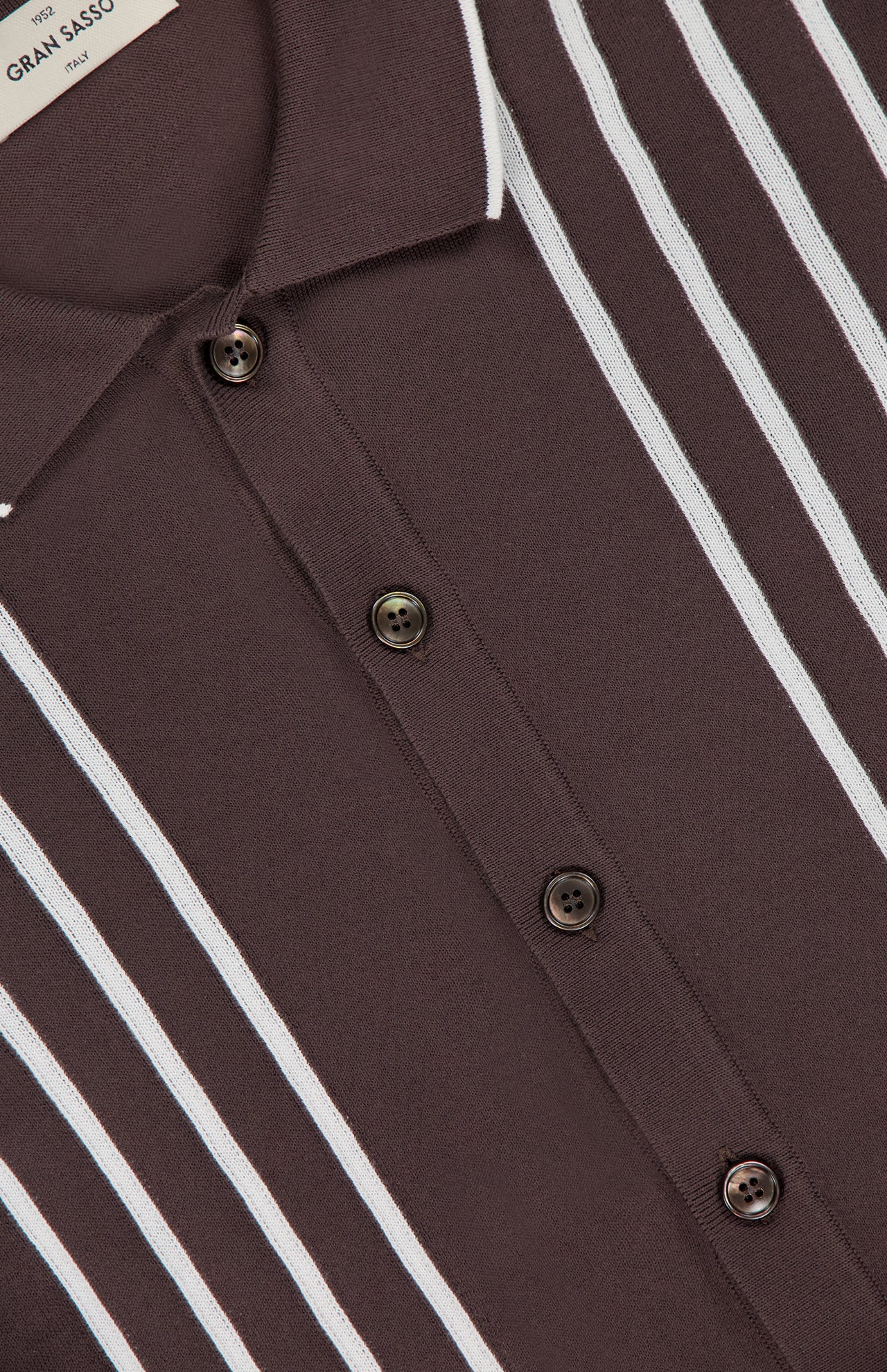 Close-up of the GRAN SASSO Button Up Knit Short Sleeve Shirt in dark brown with white vertical stripes, smooth 100% cotton fabric, and four dark front buttons. A partial label is seen at the top left.