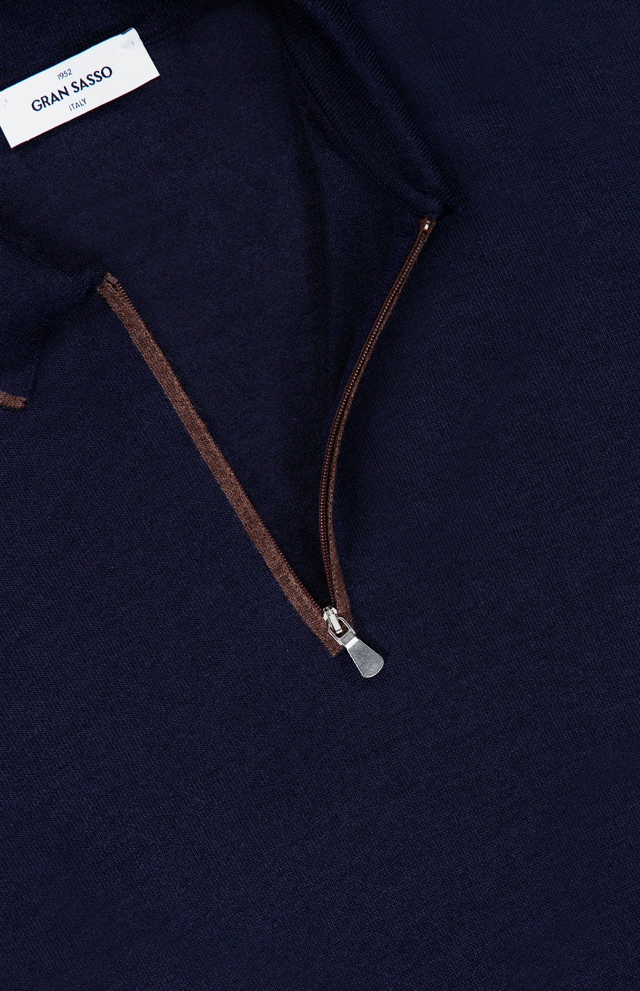 Close-up of a navy blue GRAN SASSO Quarter Zip Polo Sweater featuring a brown quarter-zip with a metal zipper pull, highlighting the collar and neck label. Expertly crafted in Italy, this sweater showcases refined craftsmanship and luxurious comfort.