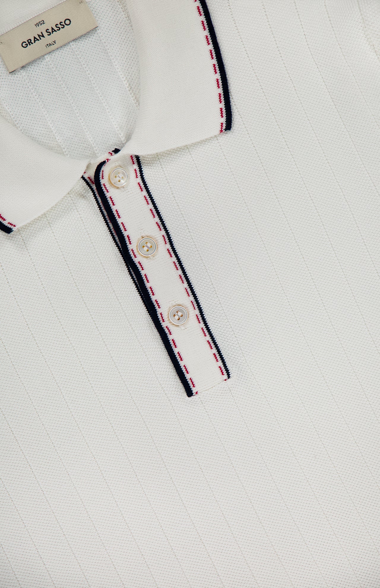 Close-up of the GRAN SASSO Stitch Detailing Polo Shirt in 100% cotton with a ribbed texture, collar, and three-button placket. Navy and red stitching trims the collar and placket; inner label reads GRAN SASSO Italy.
