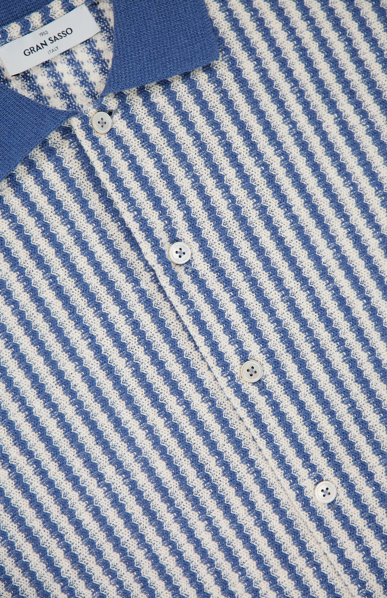 Close-up of the GRAN SASSO Stripes Short Sleeve Button Up Shirt, a retro blue and white cotton-blend polo with textured knit, diagonal stripes, blue collar, white buttons, and a Gran Sasso label inside.