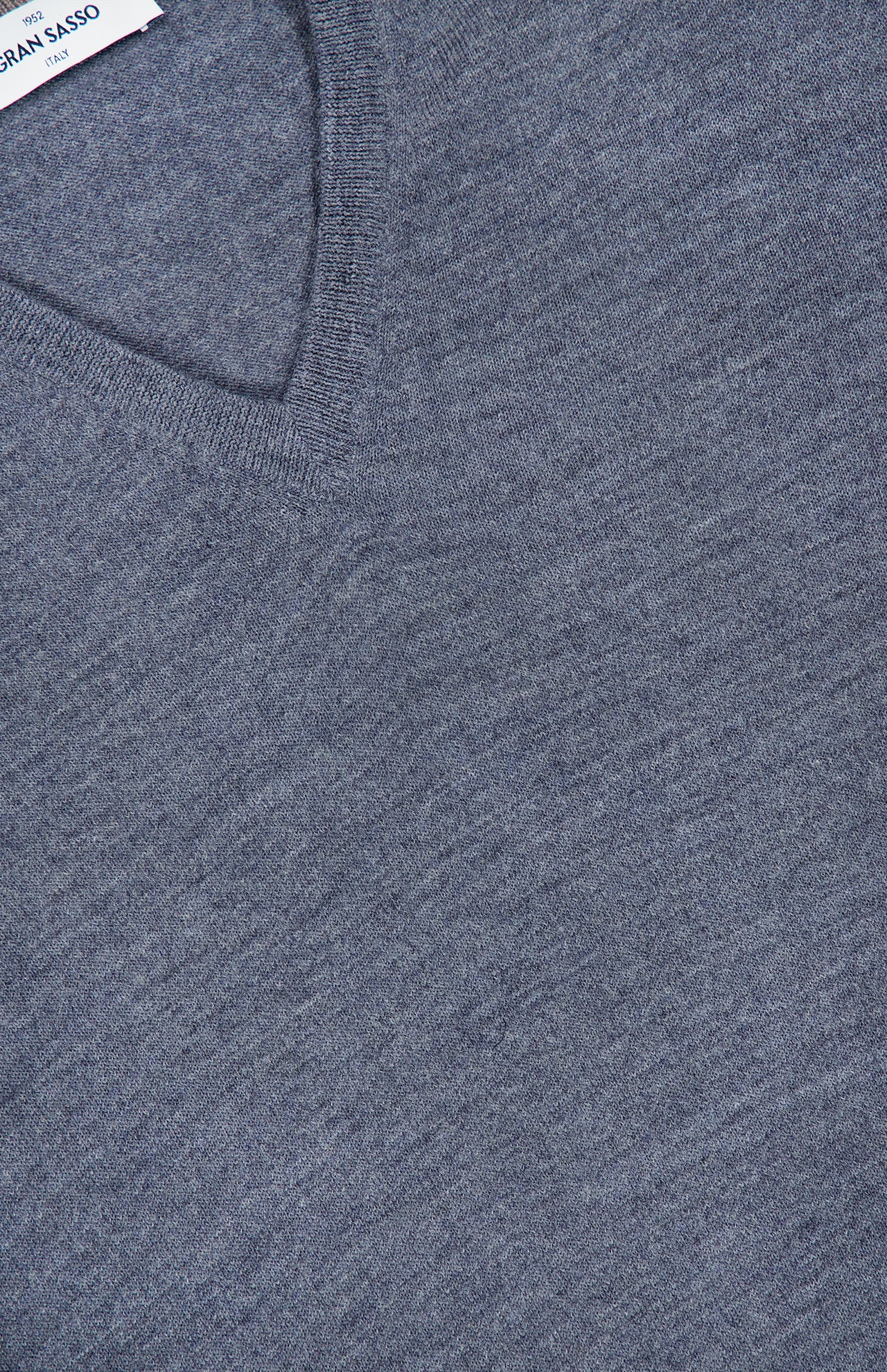 Close-up of a light grey GRAN SASSO V-Neck Virgin Wool Sweater, crafted from fine knit fabric and displaying its soft texture, with part of a white label and partial text visible in the upper left corner.