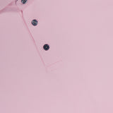 A close-up of the GREYSON Crowley Polo Shirt in light pink, featuring a collar and three black buttons on the placket, made with moisture-wicking fabric for comfort.