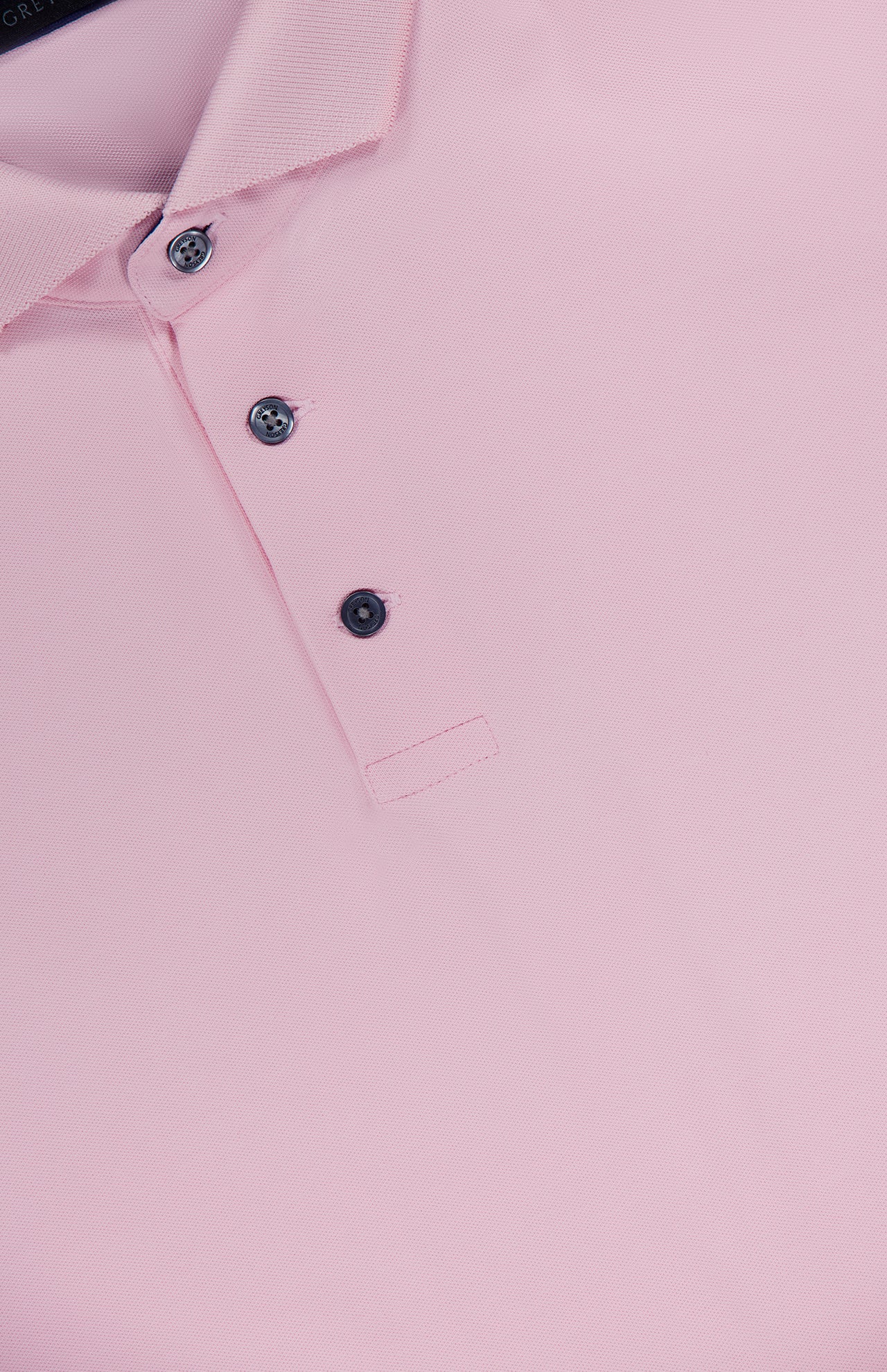 A close-up of the GREYSON Crowley Polo Shirt in light pink, featuring a collar and three black buttons on the placket, made with moisture-wicking fabric for comfort.