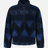 The GREYSON Guardian Sherpa Fleece Half Zip Sweater is a men’s navy blue pullover featuring a striking zigzag and abstract pattern in lighter blue shades. Designed with a quarter-zip front, long sleeves, high collar, and cozy sherpa fleece for comfort on cool days.