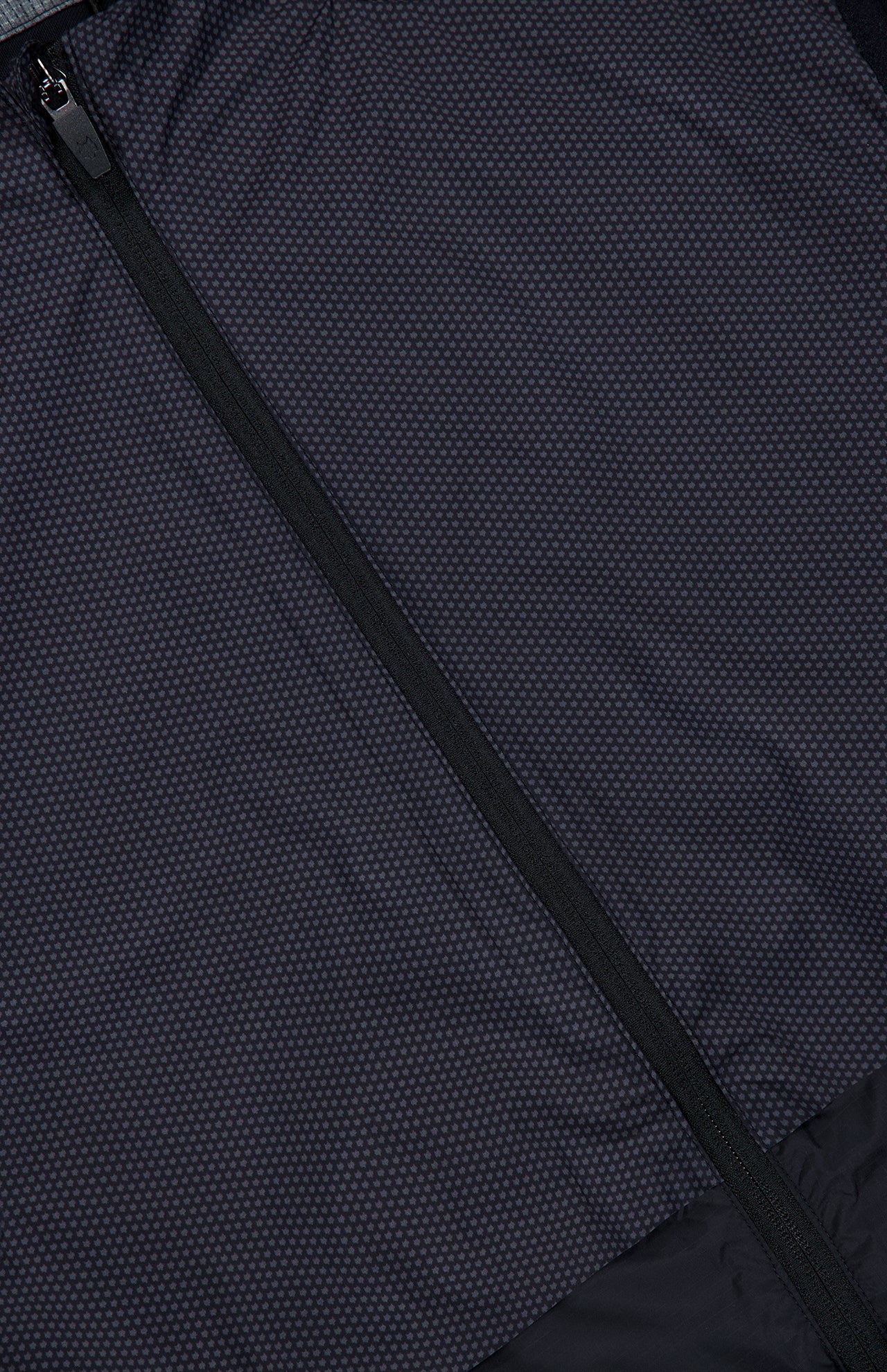 Close-up of the GREYSON Micro Icon Trailwolf Hybrid Sport Vest, showcasing its dark, subtly dotted fabric and diagonal zipper. The visible texture highlights its lightweight design, making it an ideal versatile outer layer for transitional weather.