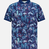 The GREYSON Night Lurk Polo Shirt is a short-sleeve, button-up performance top with a blue base and bold blue, purple, and white tropical floral print. Features solid dark blue collar/cuffs and moisture-wicking fabric for all-day comfort.