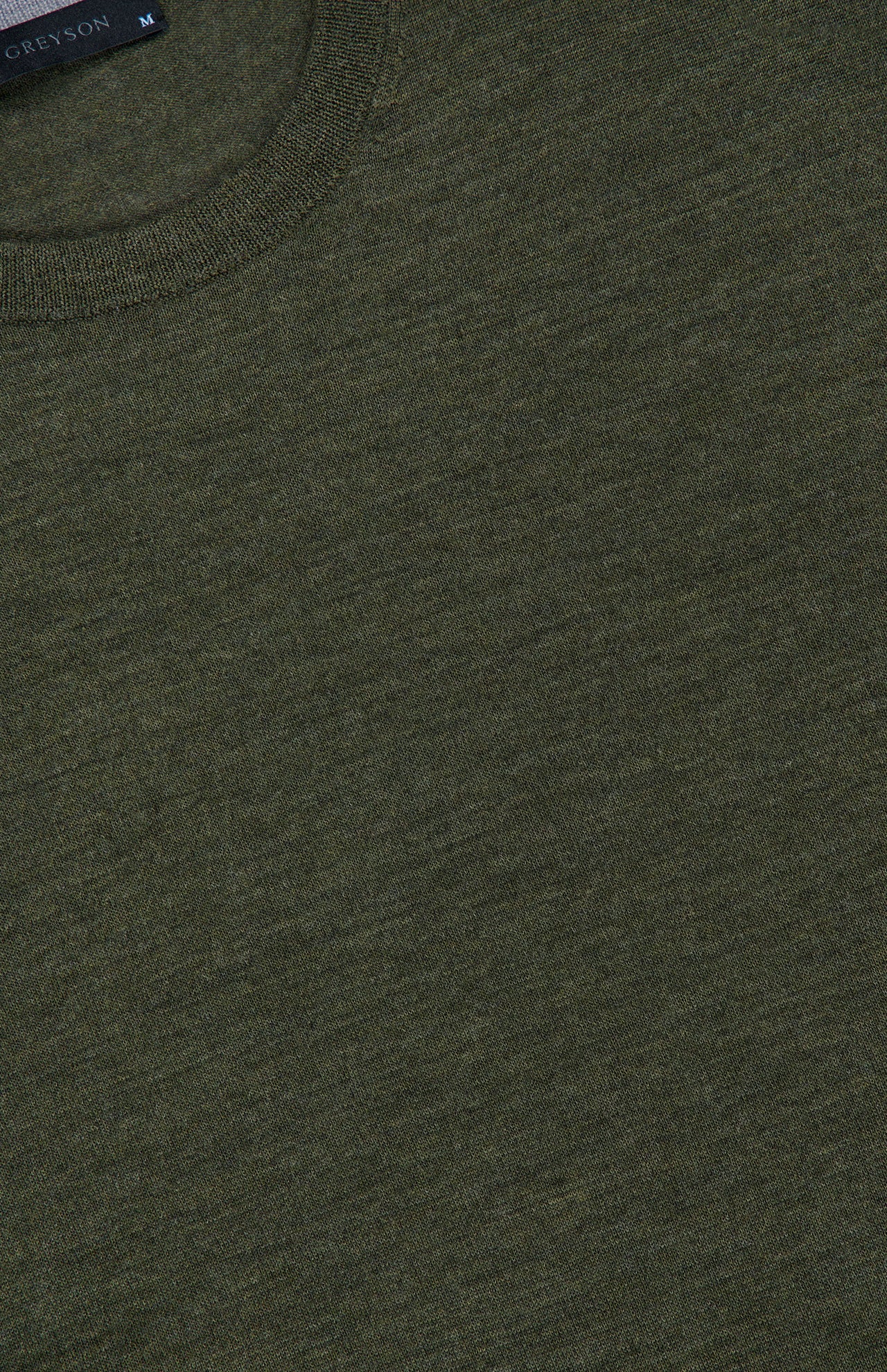 Close-up of the Saratoga Crewneck Long Sleeve Shirt by GREYSON in olive green. This men’s casual pullover features a soft, textured fabric and a comfortable fit, with a crew neckline and part of the collar tag visible at the top left.
