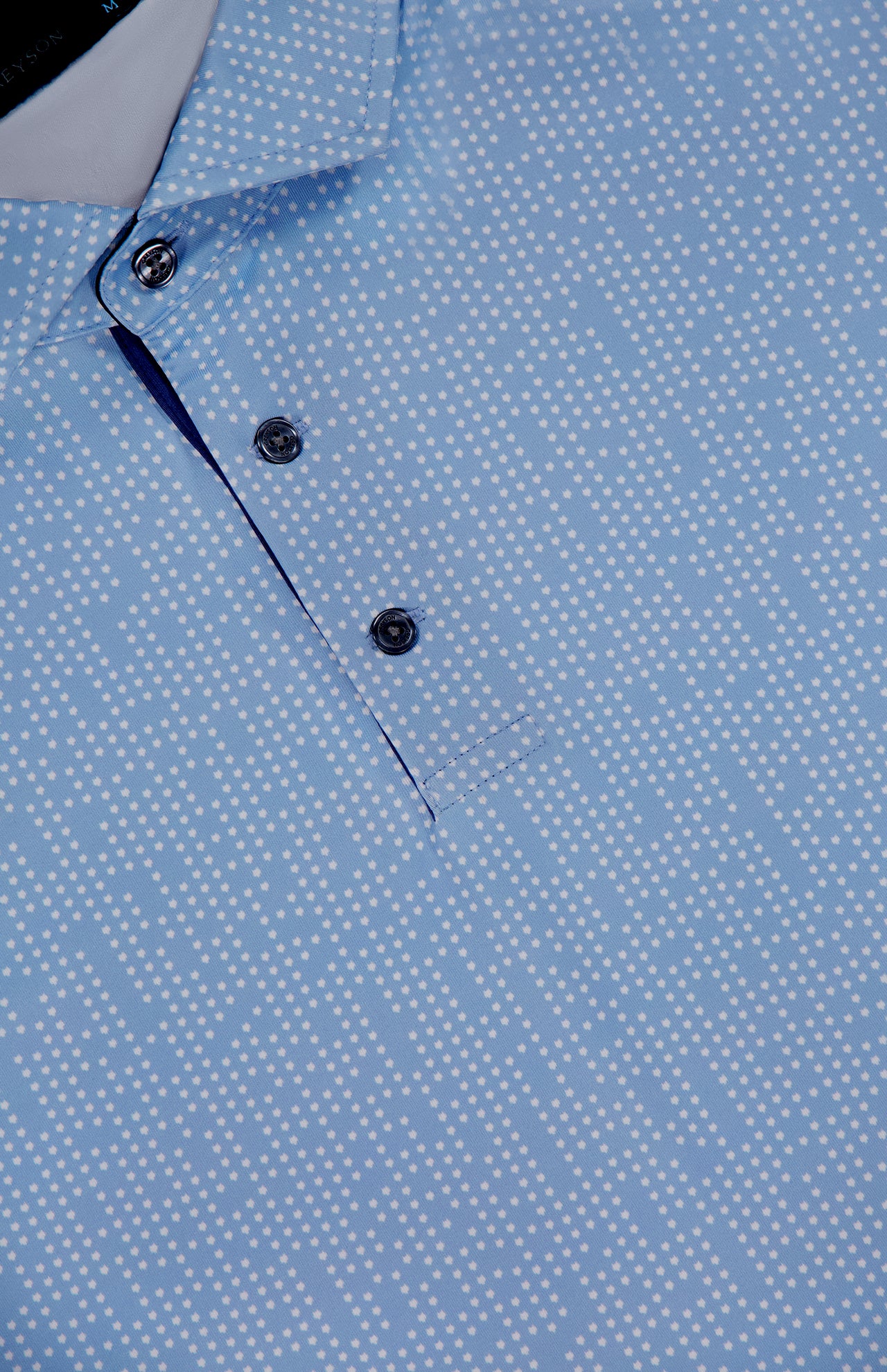 Close-up of the Silent Pact Polo Shirt by GREYSON, featuring a light blue hue, white dotted pattern, three metallic placket buttons, and built-in moisture wicking for added comfort.