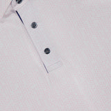 Close-up of the Silent Pact Polo Shirt by GREYSON: light pink with a subtle dotted pattern, three-button placket, and collar. Features moisture-wicking fabric for all-day comfort; inner collar tag displays the GREYSON brand.