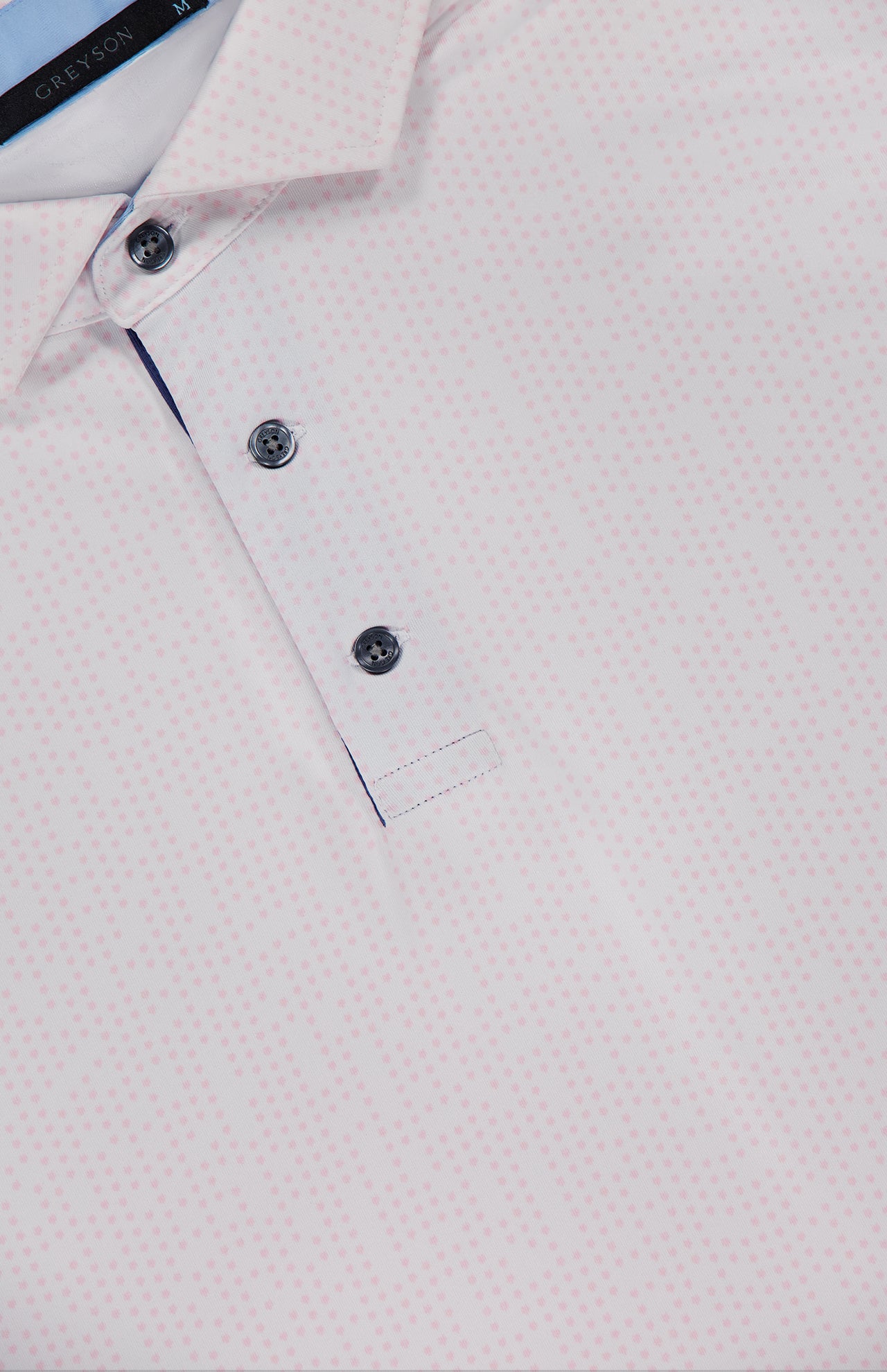 Close-up of the Silent Pact Polo Shirt by GREYSON: light pink with a subtle dotted pattern, three-button placket, and collar. Features moisture-wicking fabric for all-day comfort; inner collar tag displays the GREYSON brand.