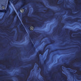 Close-up of the GREYSON Smoke In The Den Polo Shirt in blue, featuring a swirling marbled pattern and three-button placket. The collar stands out with a contrasting geometric design in light blue and white. This performance polo also provides UV protection for enhanced comfort during outdoor activities.
