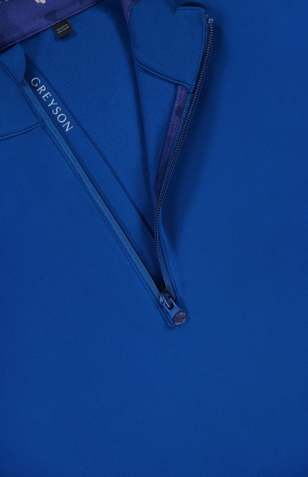Close-up of the GREYSON Tate Quarter Zip in dark blue, featuring a partially unzipped collar that reveals the brand label. Made from Italian technical fabric, its smooth finish and matching zipper pull enhance its premium appearance.
