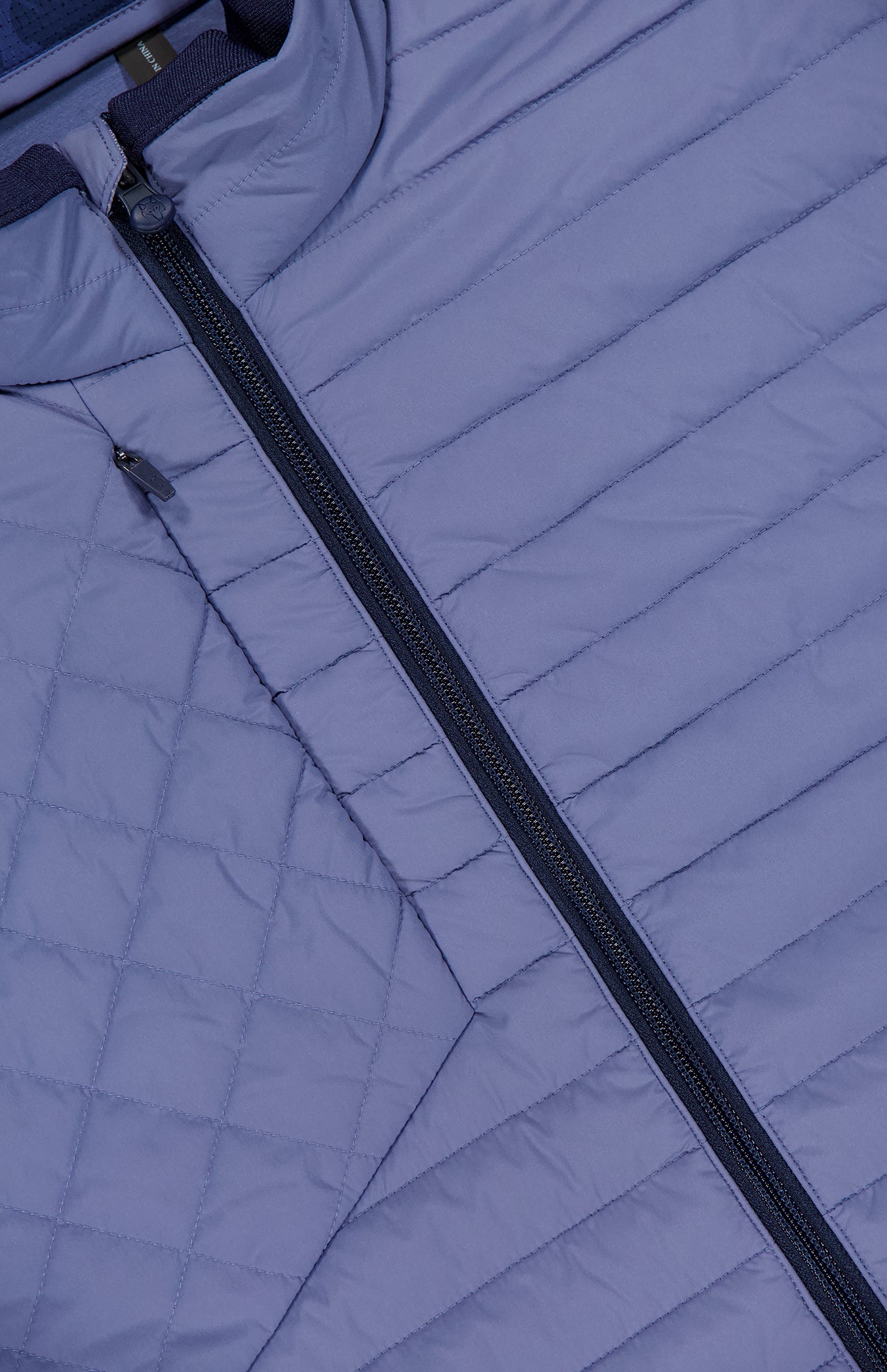 Close-up of the GREYSON Yukon Hybrid Jacket in light purple, featuring a diagonal black zipper and stitching lines that create small rectangular panels on the lightweight technical fabric.