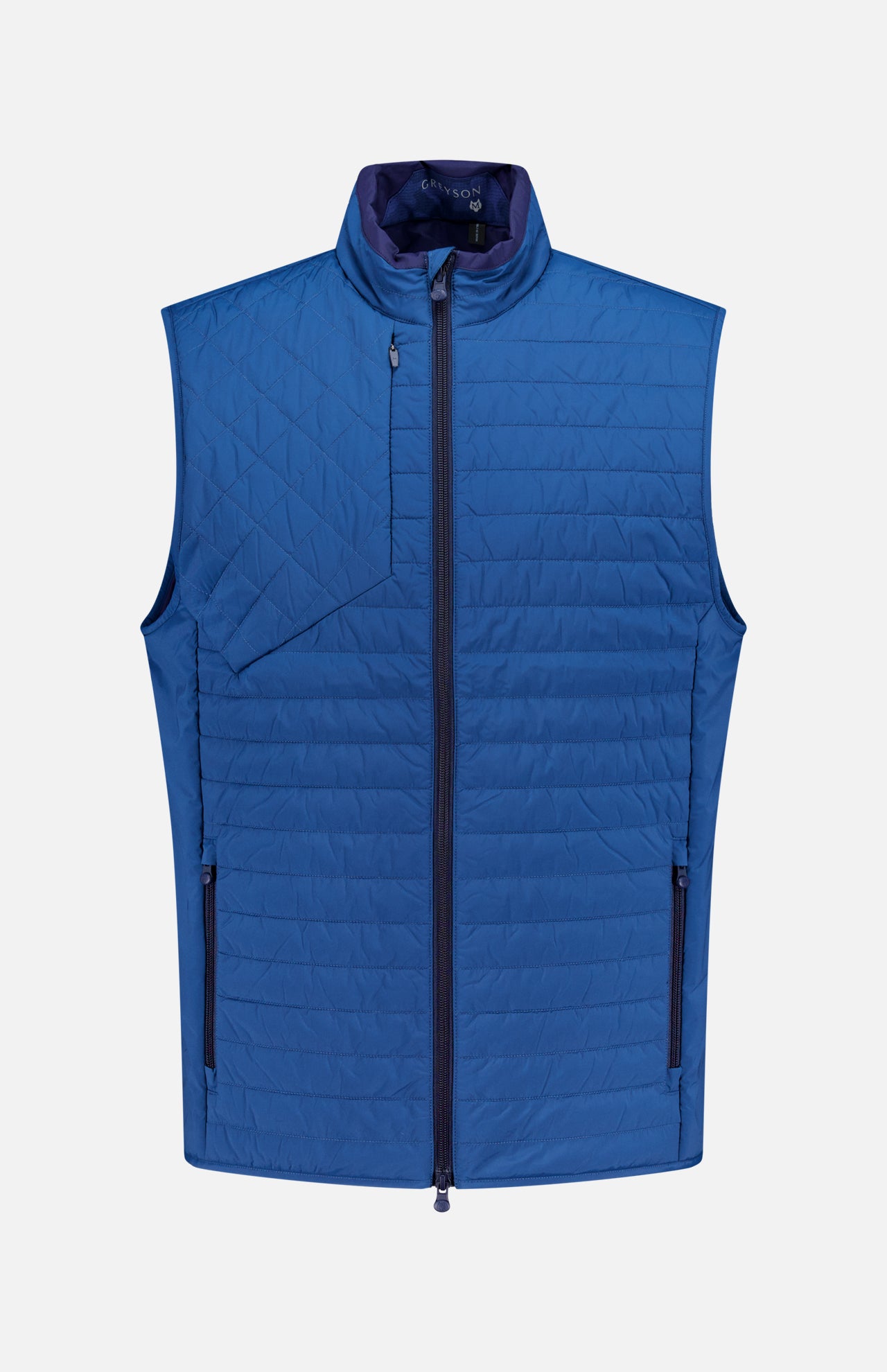 The GREYSON Yukon X-Lite Vest is a sleeveless, quilted blue hybrid vest with Primaloft insulation, featuring a front zipper, two zippered side pockets, a zippered chest pocket, and a stand-up collar. Displayed on a plain white background.