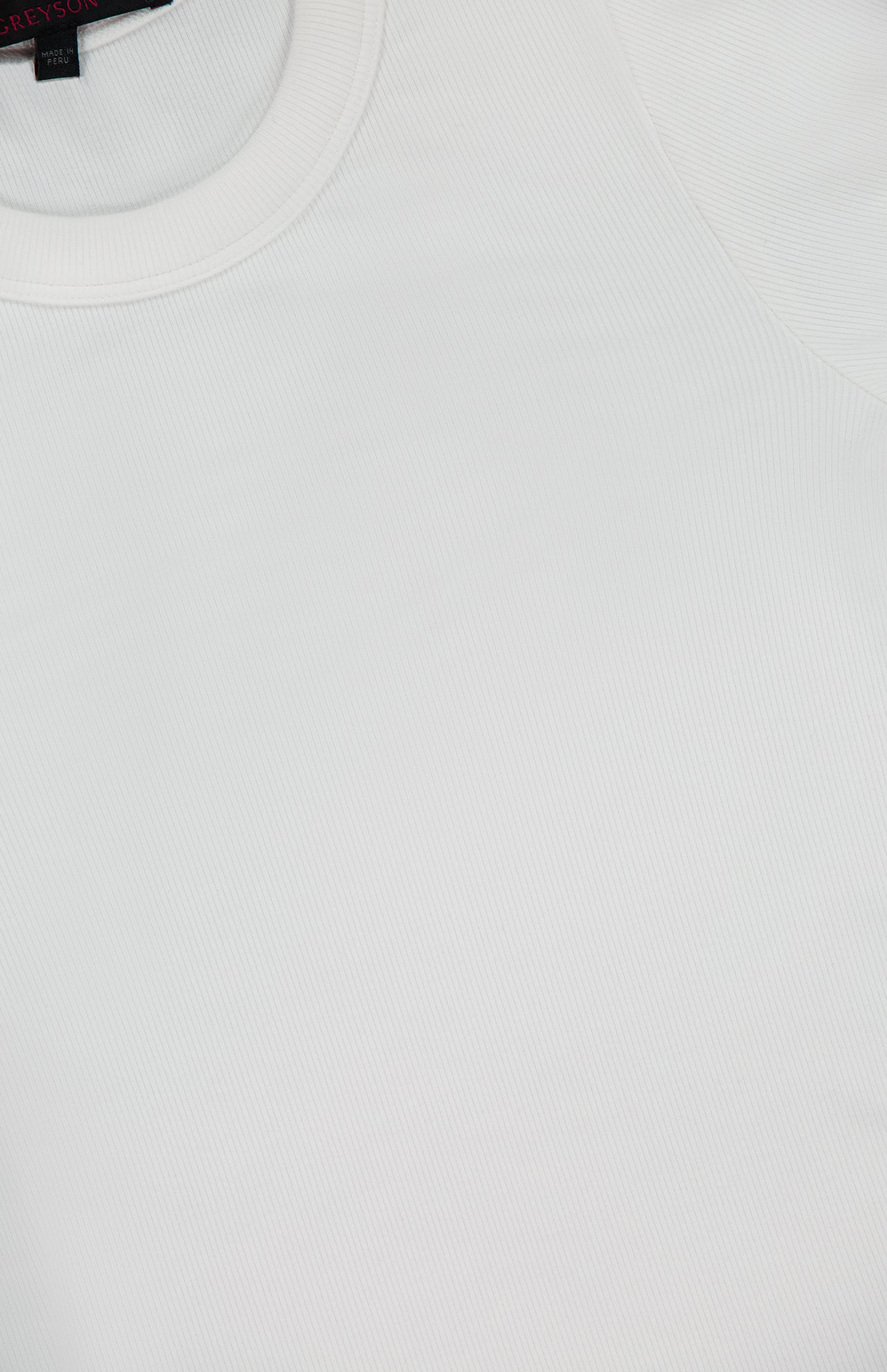 Close-up of the GREYSON Orion Long Sleeve in plain white, featuring a slim fit, smooth fabric texture, and classic crew neckline; a portion of the black clothing label is visible in the upper left corner.