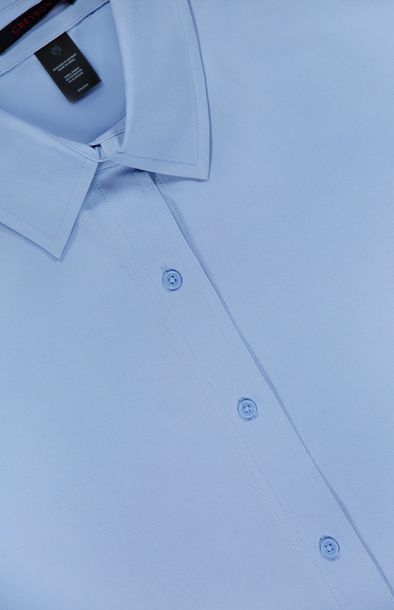 Close-up of the GREYSON Ashe Button Down Shirt in light blue, featuring a neatly pressed collar and three buttons on the front placket. The fabric appears smooth and crisp.