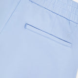 Close-up of the Ojai Trouser Short by GREYSON in light blue, showing an elastic waistband, welt pocket, and a small embroidered G logo above the right-side pocket.