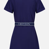 The Phoenix Belted Shirt Dress by GREYSON is a navy blue, short-sleeve mini dress shown from the back, featuring a collar and a matching navy belt emblazoned with the GREYSON logo in white. Made from Italian stretch fabric, this technical shirt dress offers a slightly flared skirt and cuffed sleeves for a refined yet comfortable style.