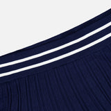 The GREYSON Pointelle Mini Skirt is shown in close-up against a plain white background. Crafted from pleated dark blue fabric, it features a ribbed waistband with two parallel white stripes. The quick-dry material and built-in undershort deliver comfort and practicality for all-day wear.