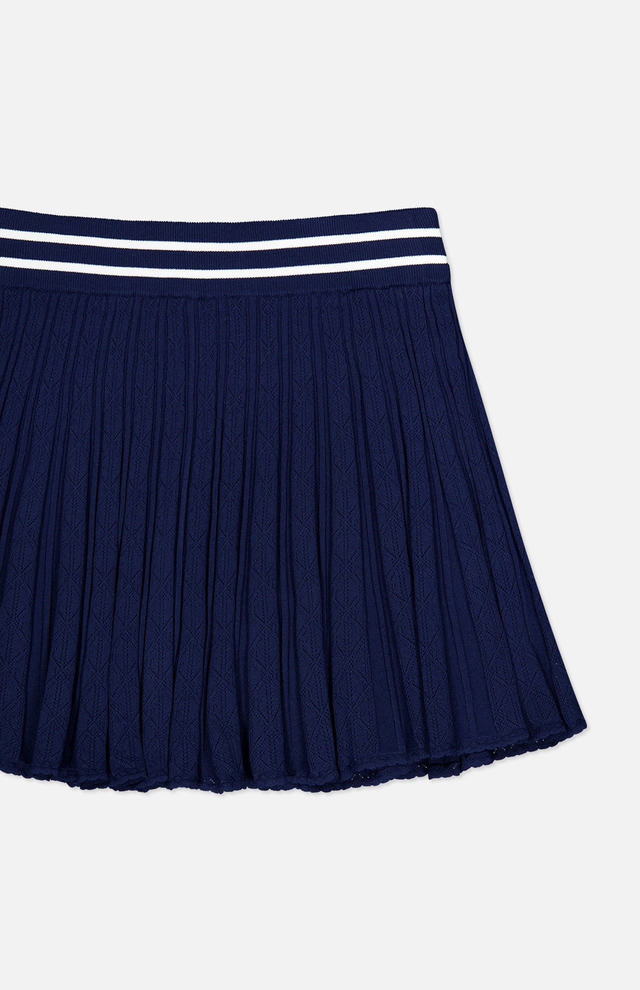 The GREYSON Pointelle Mini Skirt is a navy blue pleated skirt featuring a textured pointelle pattern and a waistband with two white horizontal stripes, designed with a built-in undershort for added comfort, shown against a white background.