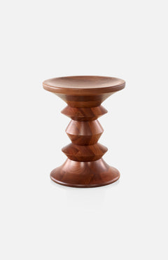 The HERMAN MILLER Eames Turned Stool in Walnut (Floor Model) features a smooth, round top and base with a central stack of angular geometric forms, all elegantly crafted from rich, polished walnut.