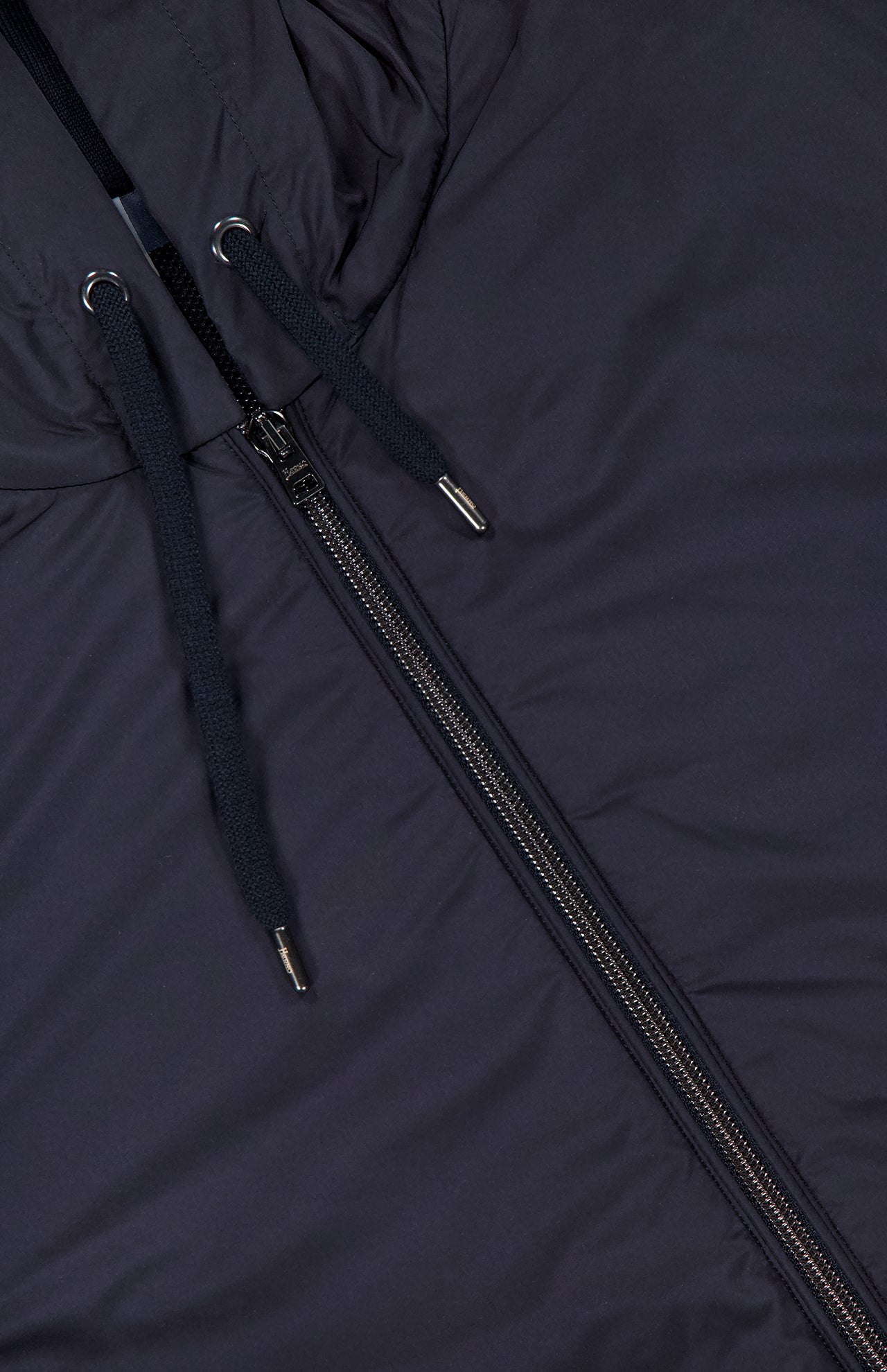 Close-up of the HERNO Cotton Pique Nylon Front Zip Hooded Bomber Jacket in a dark shade, featuring a smooth, slightly shiny fabric, zipper, partial hood, and two black drawstrings with metal tips—ideal for lightweight layering.
