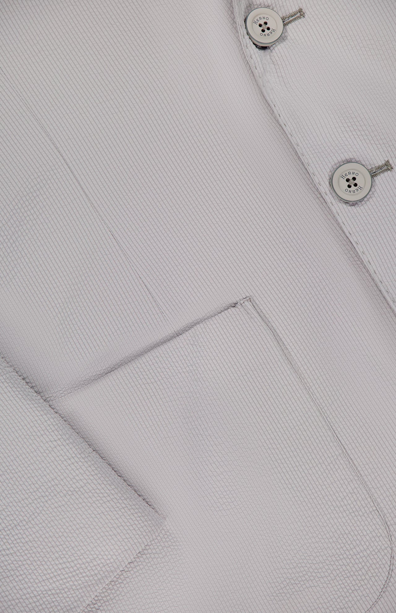 Close-up of HERNO's Seersucker 2 Button Blazer for men in light grey, highlighting two buttons, a lapel, front pocket, and a subtle woven texture for an elegant finish.