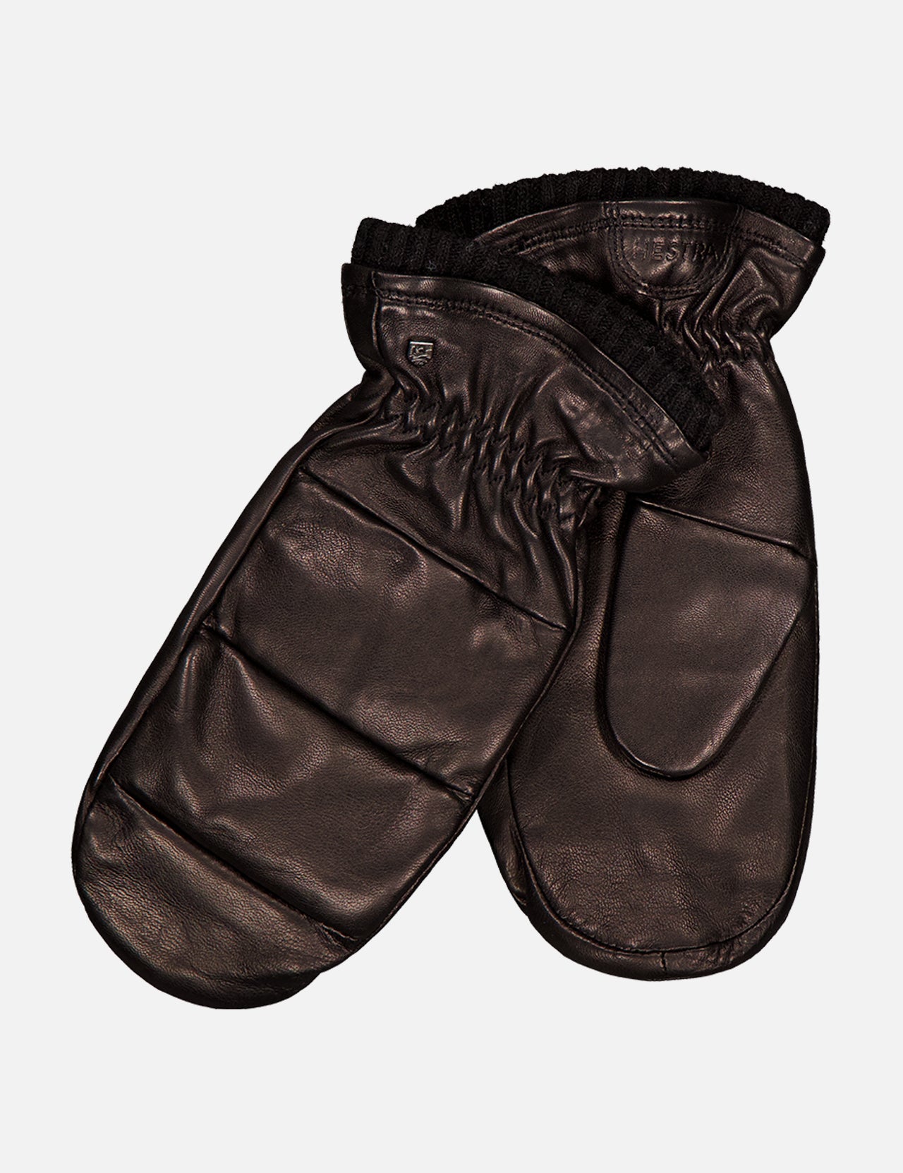 A pair of HESTRA Torun Mittens in dark brown hairsheep leather, featuring elasticized wrists and a smooth, shiny finish, shown overlapping on a plain white background.