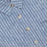 Close-up of the HEVRON Katja Cropped Linen Top, featuring blue and white vertical stripes, five light buttons, two visible pockets, and a textured lightweight linen fabric.