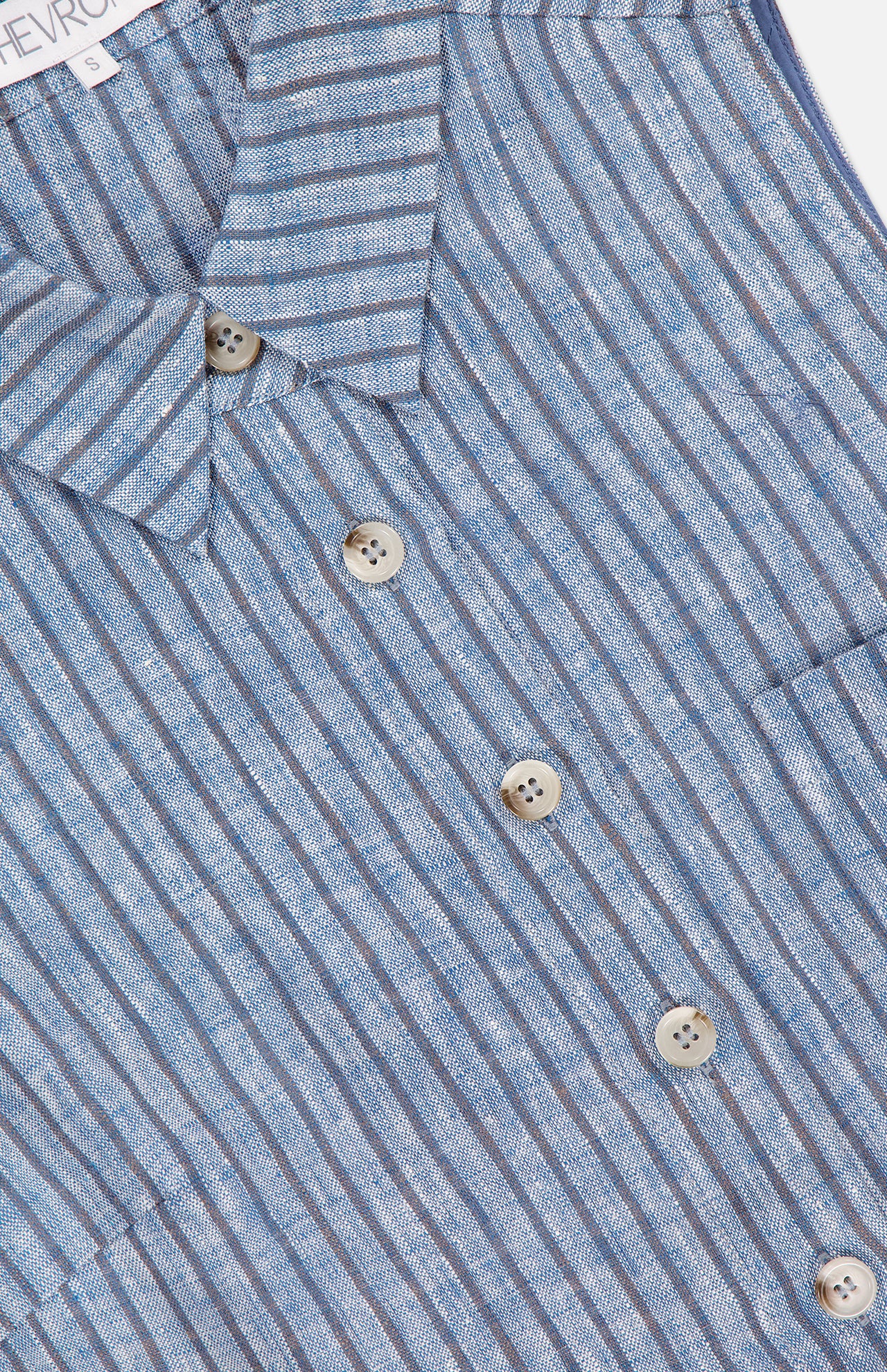 Close-up of the HEVRON Katja Cropped Linen Top, featuring blue and white vertical stripes, five light buttons, two visible pockets, and a textured lightweight linen fabric.