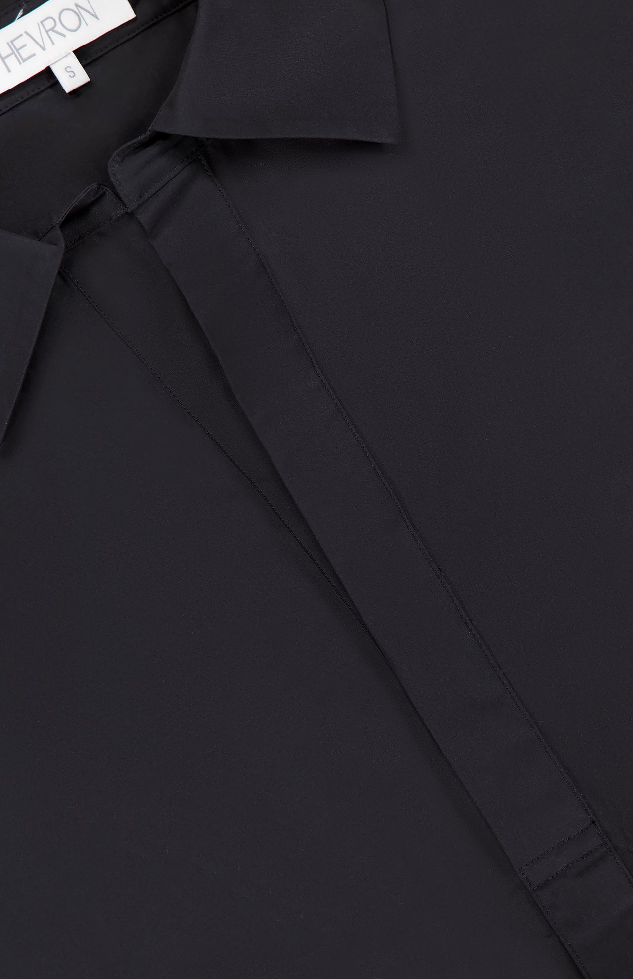 Close-up of the Paola Adjustable Front Top by HEVRON, featuring a hidden button placket, adjustable epaulette detail, and a glimpse of a white label at the neckline.
