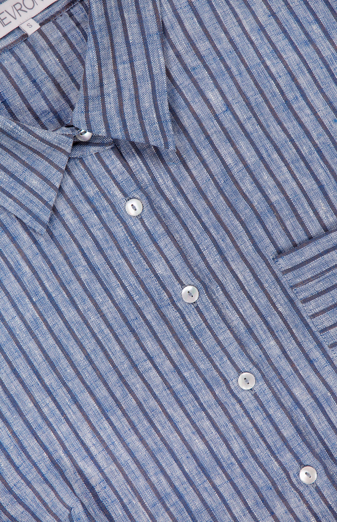 Close-up of the HEVRON Raquel Pleated Sleeves Top in blue stripes, featuring a button-front, visible collar, front buttons, right-side pocket, and textured linen fabric.