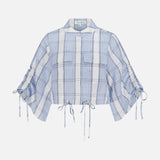 The HEVRON Eva Linen Cropped Top is a light blue and white plaid linen top featuring two front pockets, short ruched drawstring sleeves, and adjustable drawstrings at the hem and sleeves, shown against a white background.