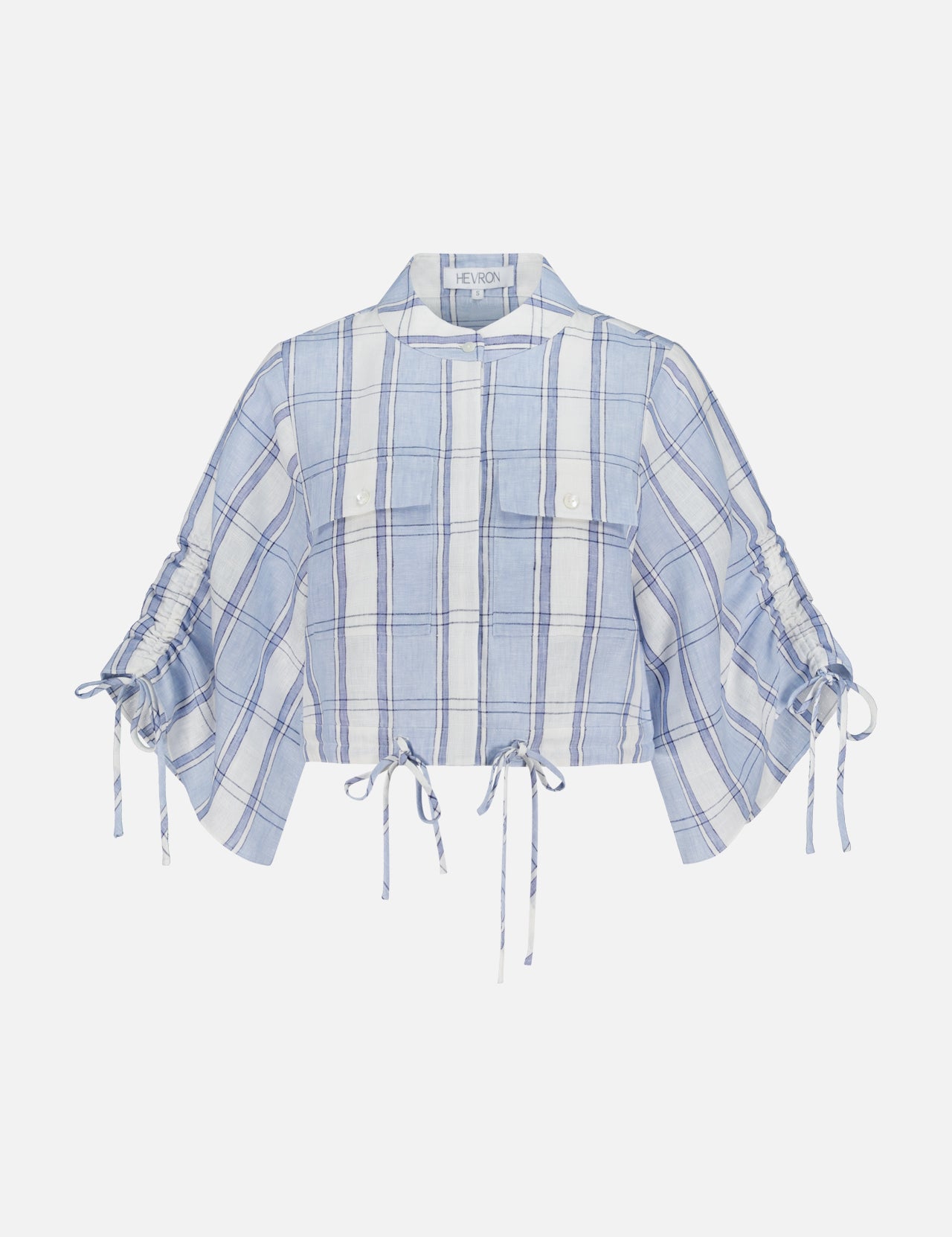 The HEVRON Eva Linen Cropped Top is a light blue and white plaid linen top featuring two front pockets, short ruched drawstring sleeves, and adjustable drawstrings at the hem and sleeves, shown against a white background.