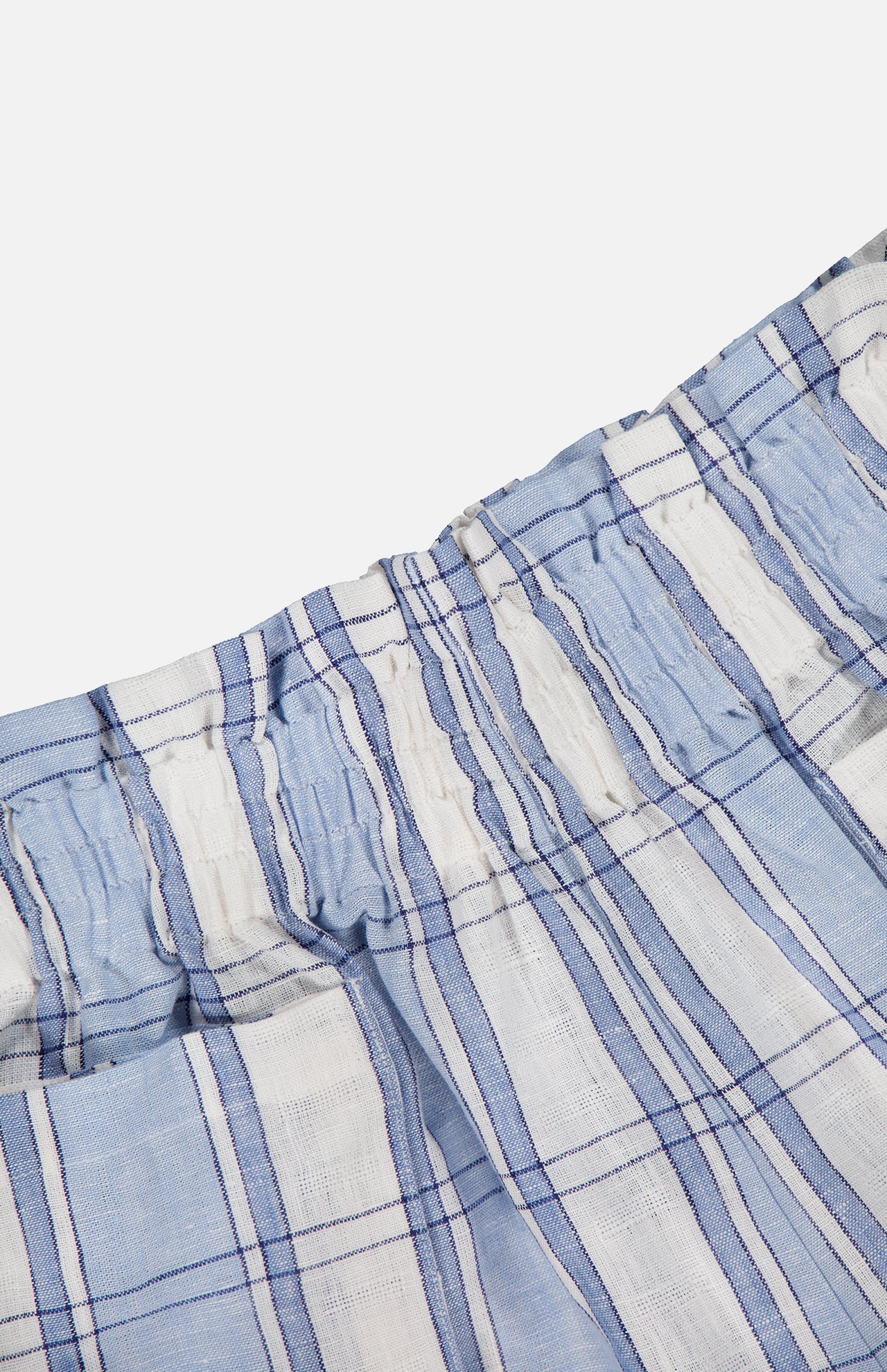 Close-up of HEVRON's Mira Plaid Linen Short, featuring lightweight, breathable linen with a light blue and white plaid pattern, thin dark blue stripes, and an elastic waistband.