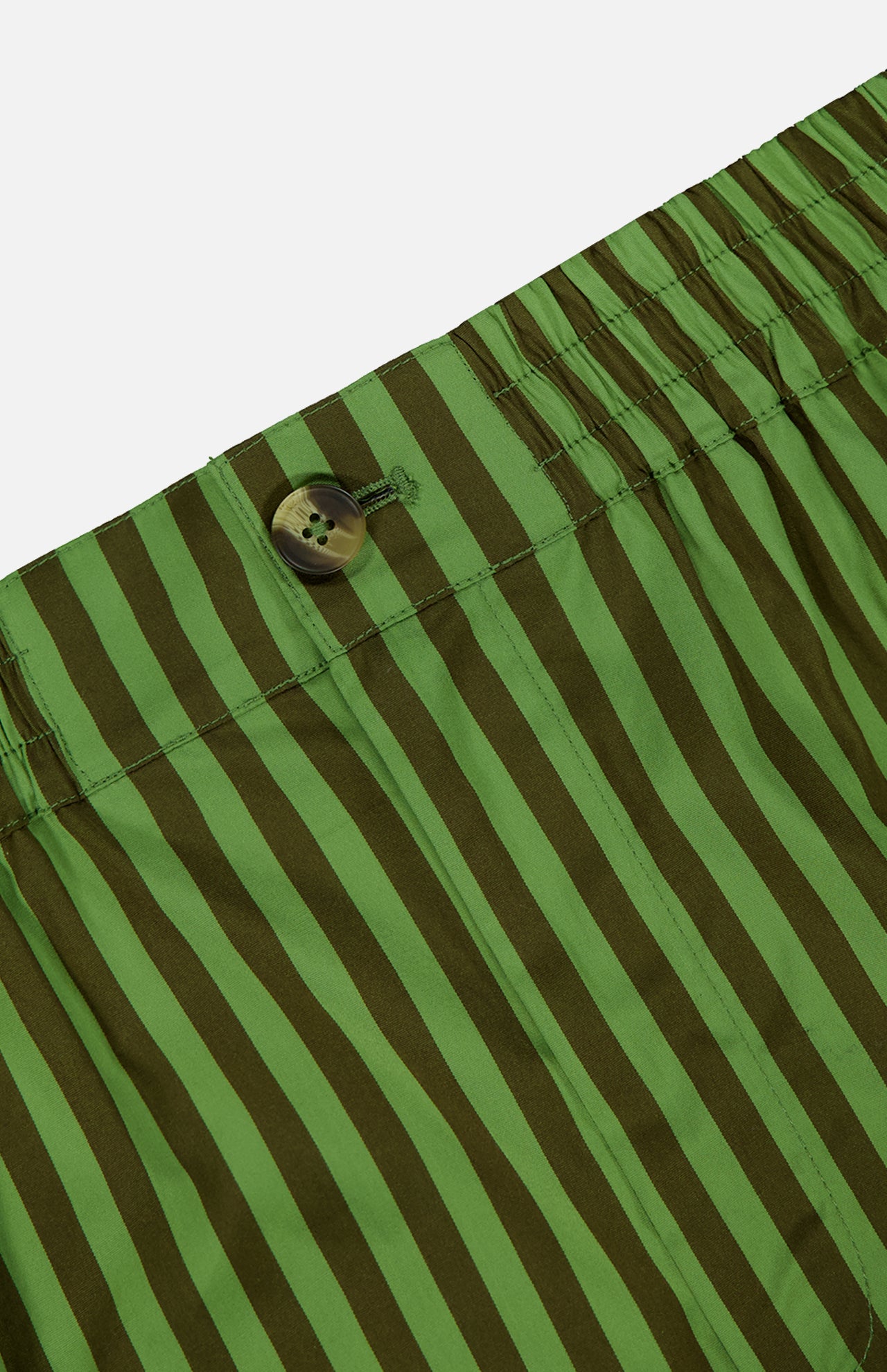 Close-up of the Remi Stripe Shorts by HEVRON, featuring green and dark green vertical stripes, a button, and an elastic waistband—perfect for a summer set.